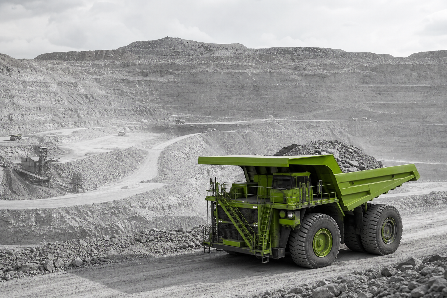 A green ultra-class haul truck operating in a monochrome open-pit mine
